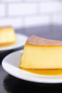 Delicious caramel flan slice on a white plate, showcasing smooth texture and rich syrup.
